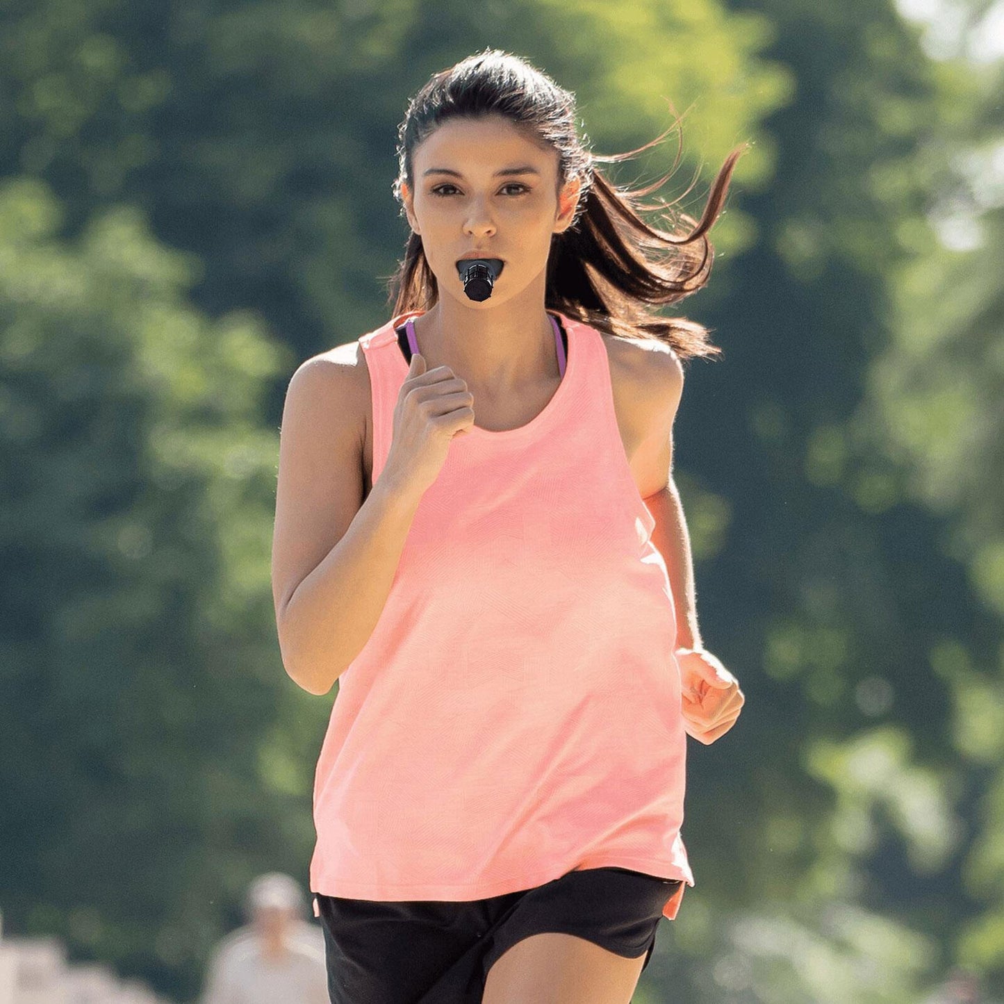 Breathing trainer foregrounded while athlete in the background runs or cycles, to suggest how respiratory training supports endurance sports performance.